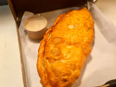 A donair pocket in its box with a cup of donair sauce